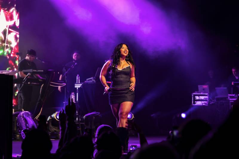 A person with long hair on stage in an indoor venue in front of a large crowd.