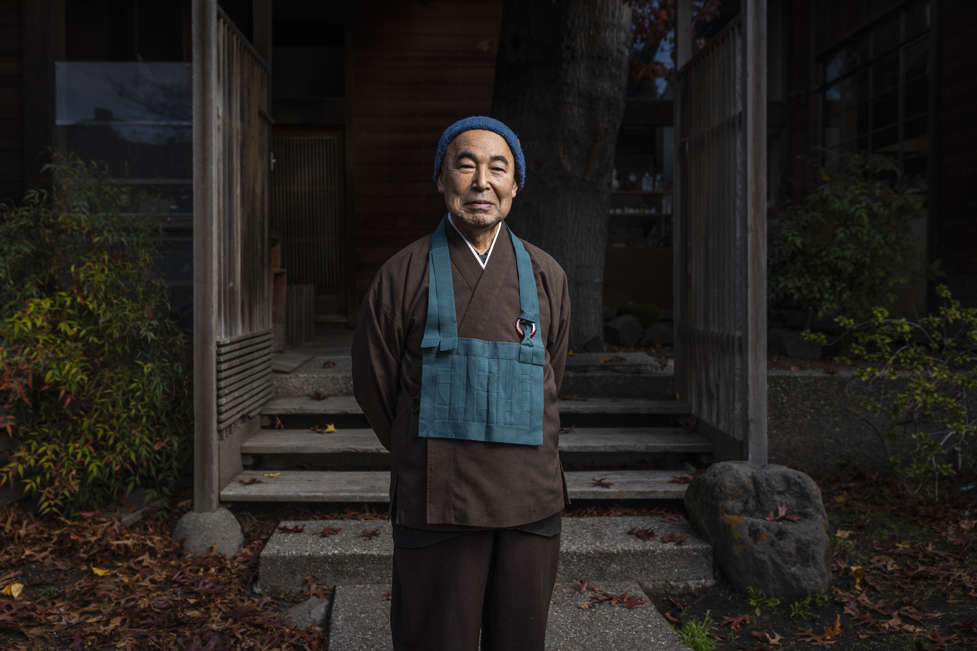A person wears brown and blue clothing outside a wooden building.