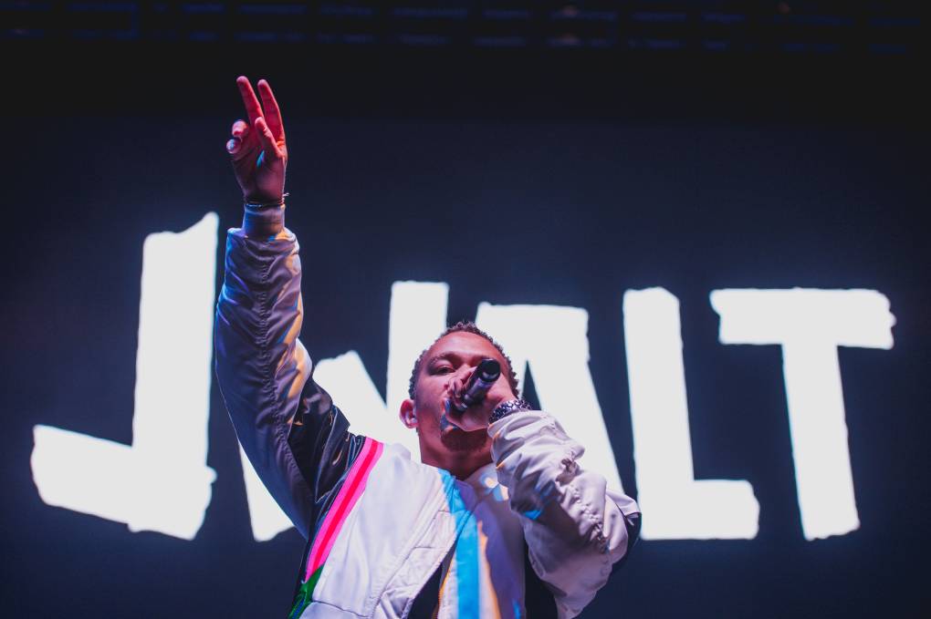 a rap performer stands on stage with a microphone and a hand in the air