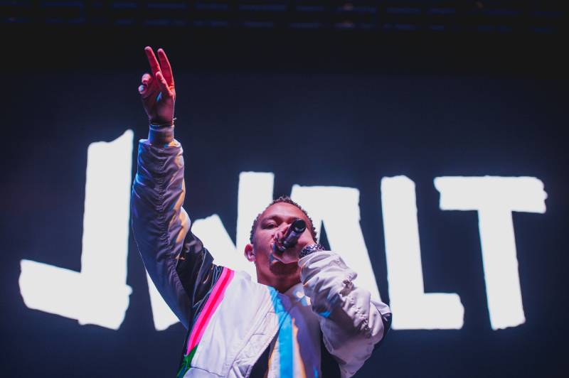 a rap performer stands on stage with a microphone and a hand in the air