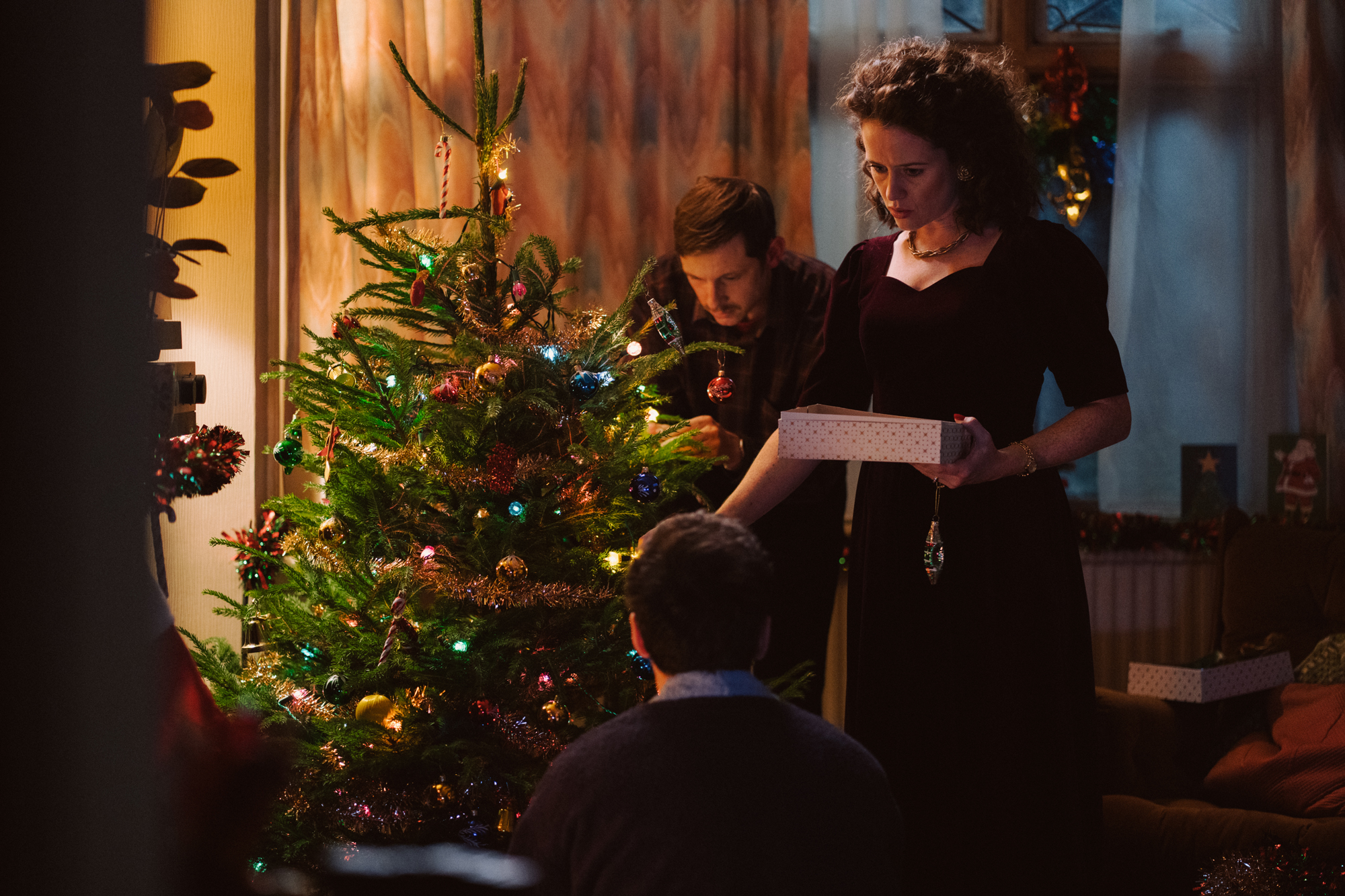 Man and woman decorate a Christmas tree with a third figure seated in front of them