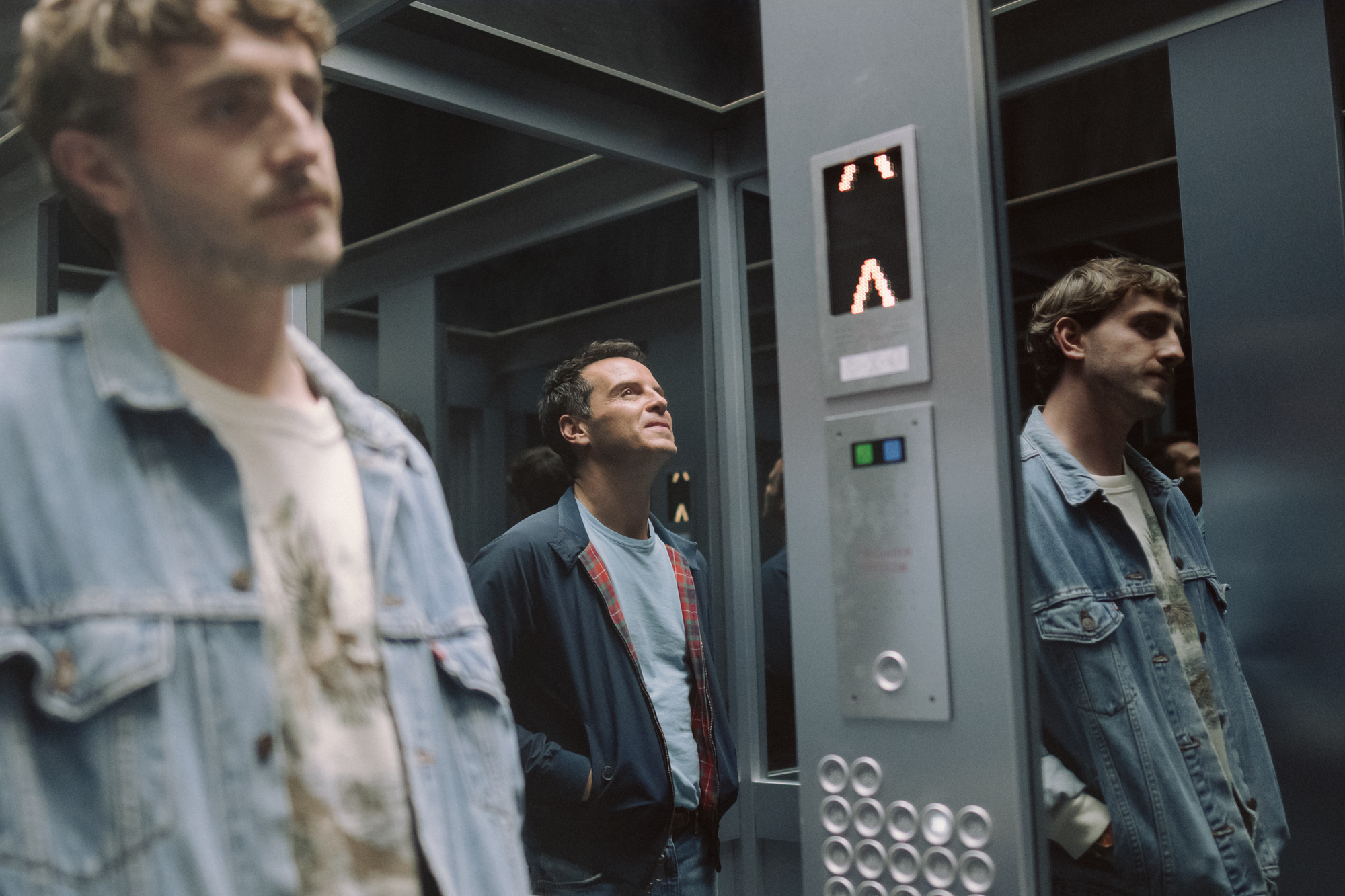 Two men stand in elevator, one reflected in mirror