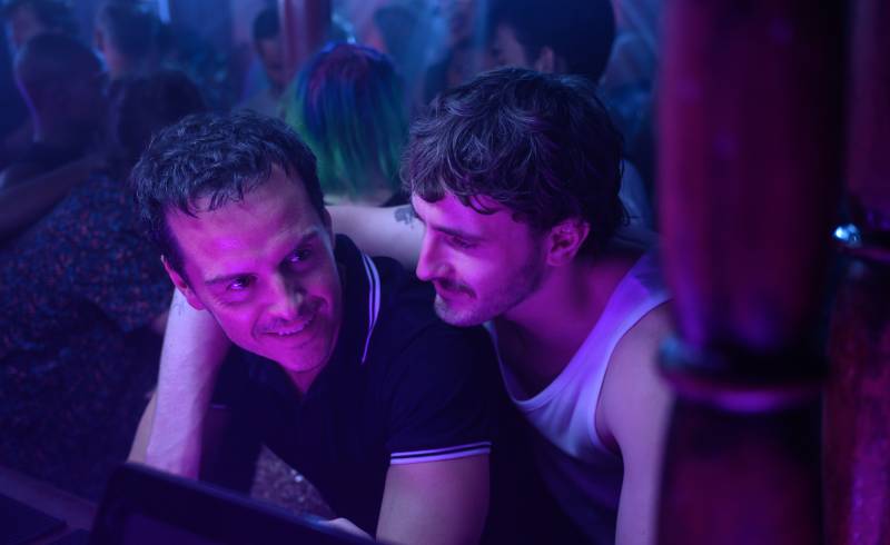 One man drapes arm over other man's shoulders in club lit by pink light