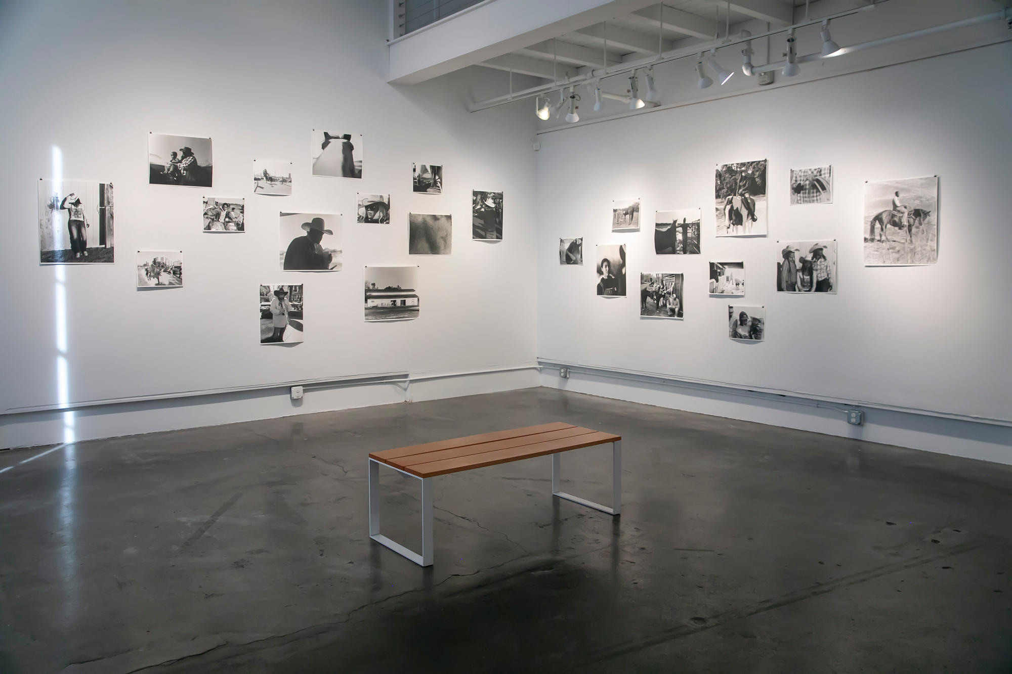 Black and white photo prints arranged in loose salon style unframed on two white gallery walls