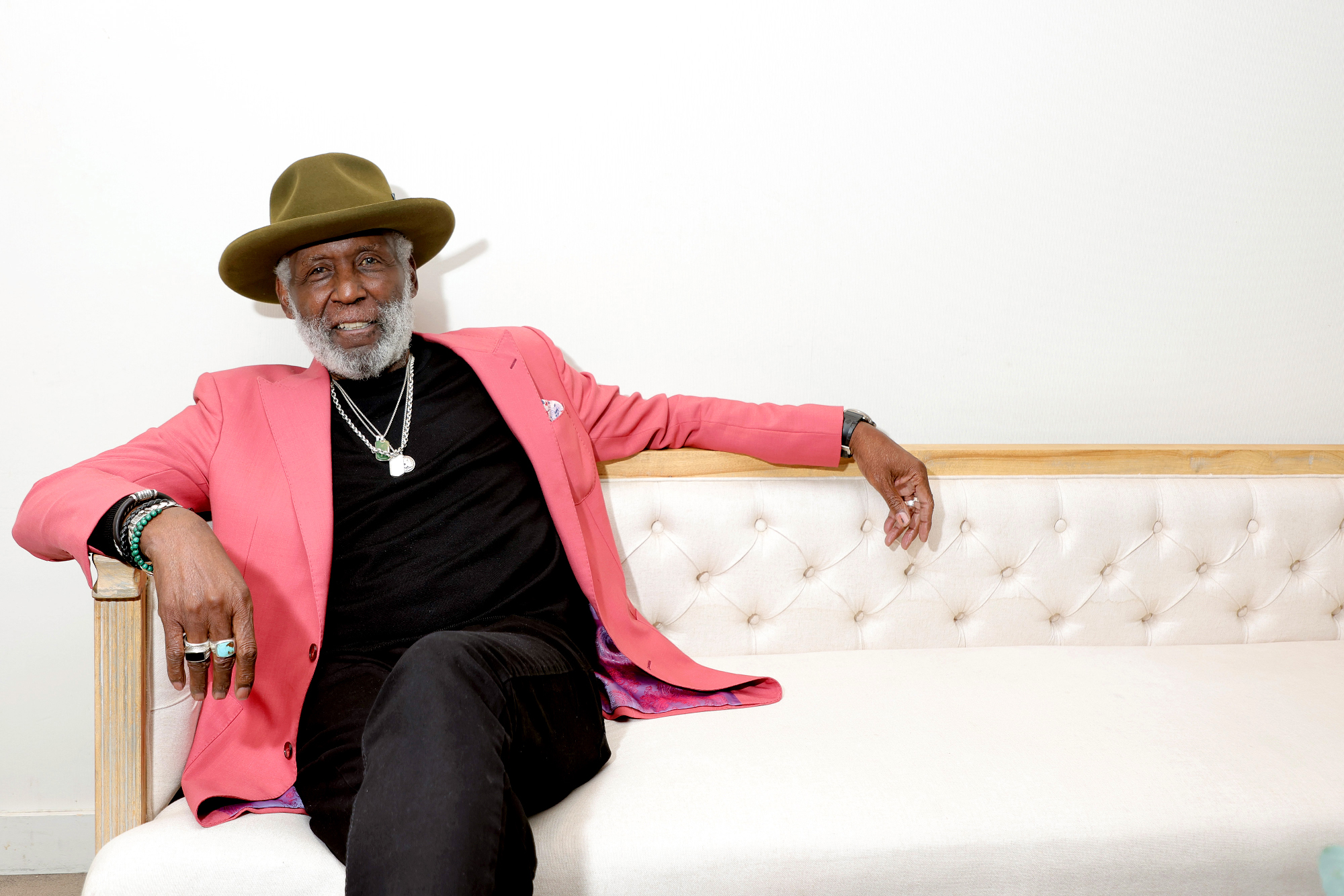 Man in hat and pink suit jacket leans on white couch