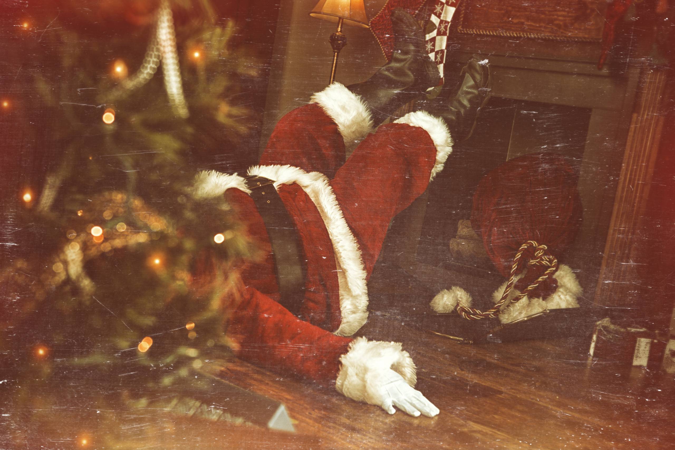 A Santa lying on the floor, arms spread wide, with his feet resting above a fireplace.