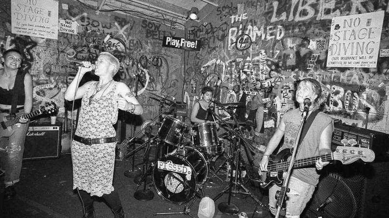 a black and white photo of a punk trio, all women, performing in a punk club