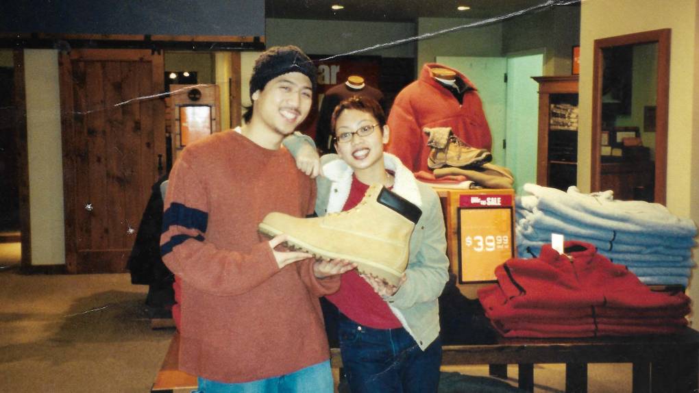 A young man and woman pose for a photo inside a clothing store while holding a oversized Timberland work boot.