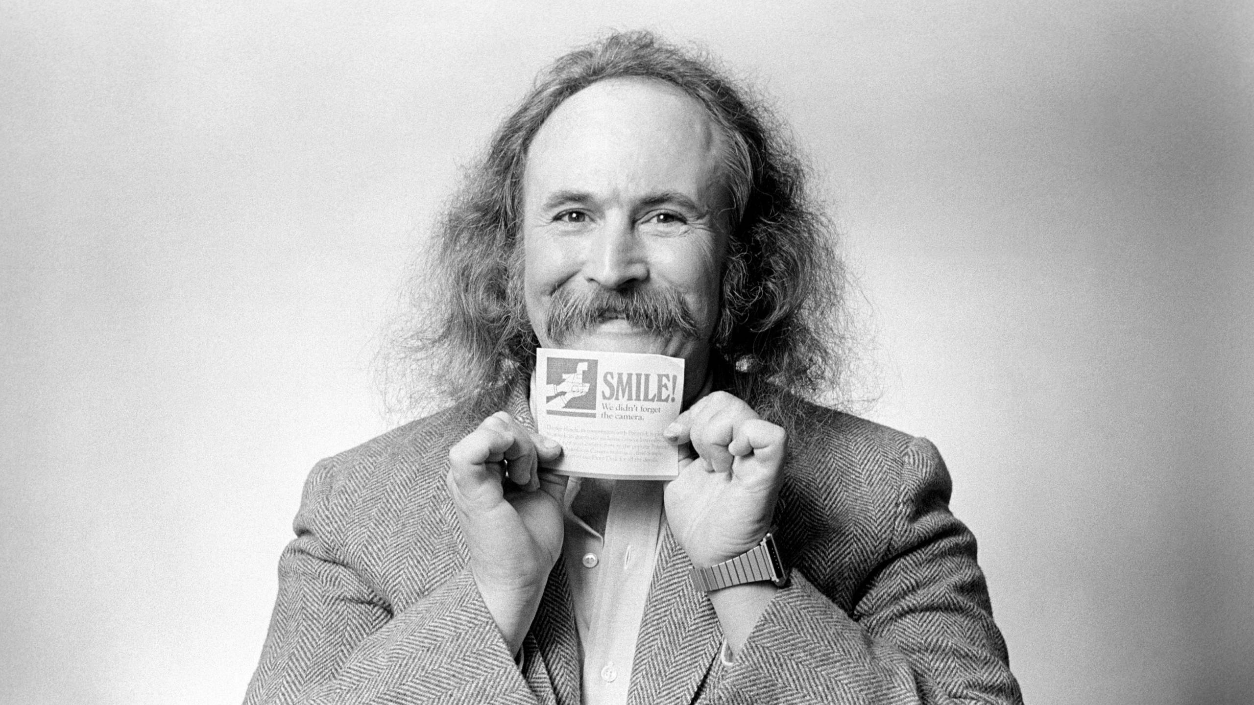 Black and white photo of man with mustache holding a card that says  "smile" below his smiling mouth