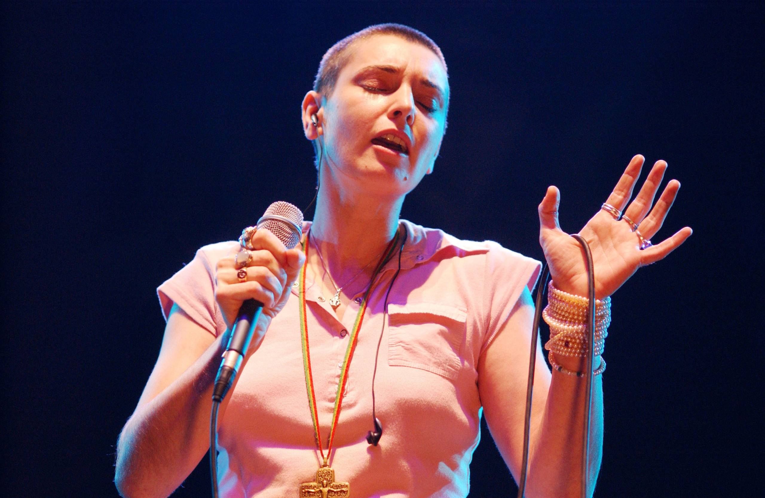 Woman with shaved hair in pink polo shirt sings with eyes closed