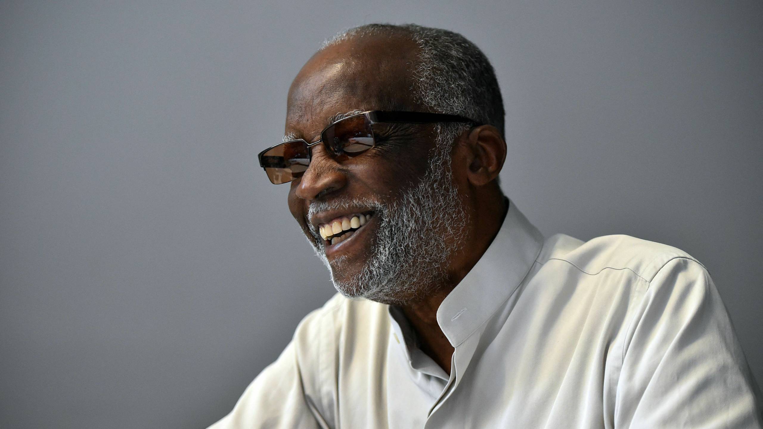 Black man in sunglasses and white shirt smiles