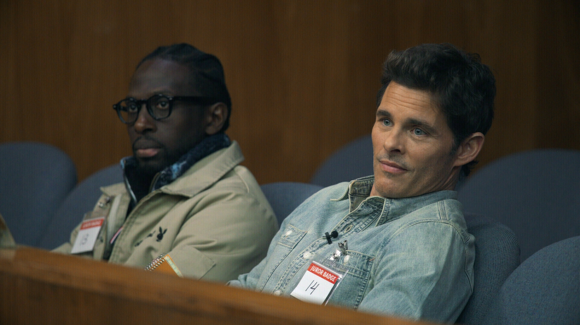 A Black man and a white man sit side-by-side in a jury box.