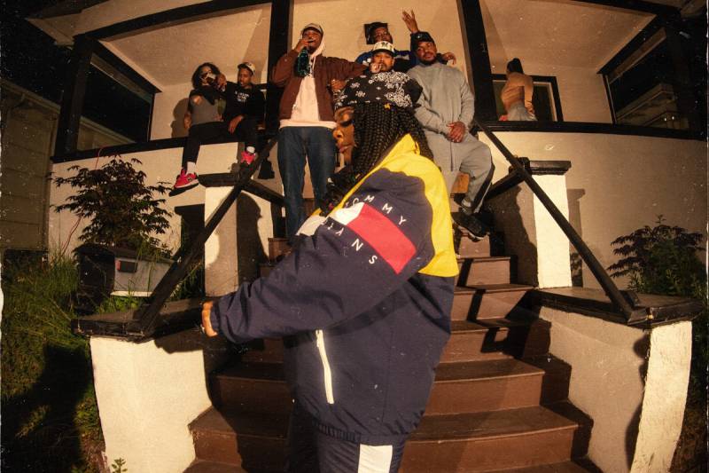 The album cover of Kamaiyah's 'Another Summer Night' shows her in a vintage Tommy Hilfiger jacket, standing outside of a house party.