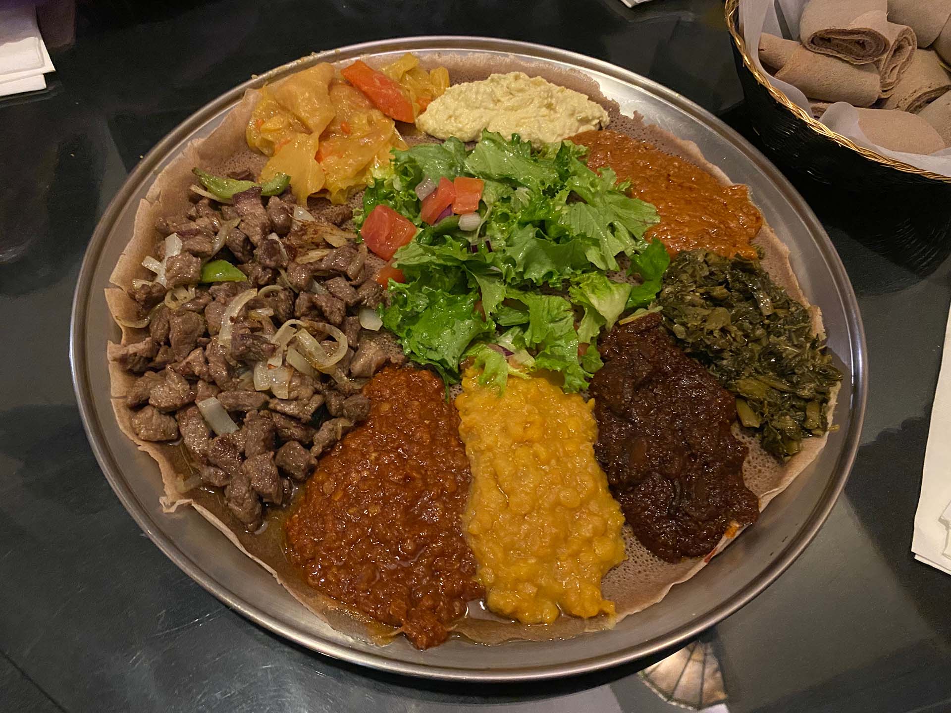 A colorful spread of Ethiopian stews and sautes, served on an injera-lined round metal platter.