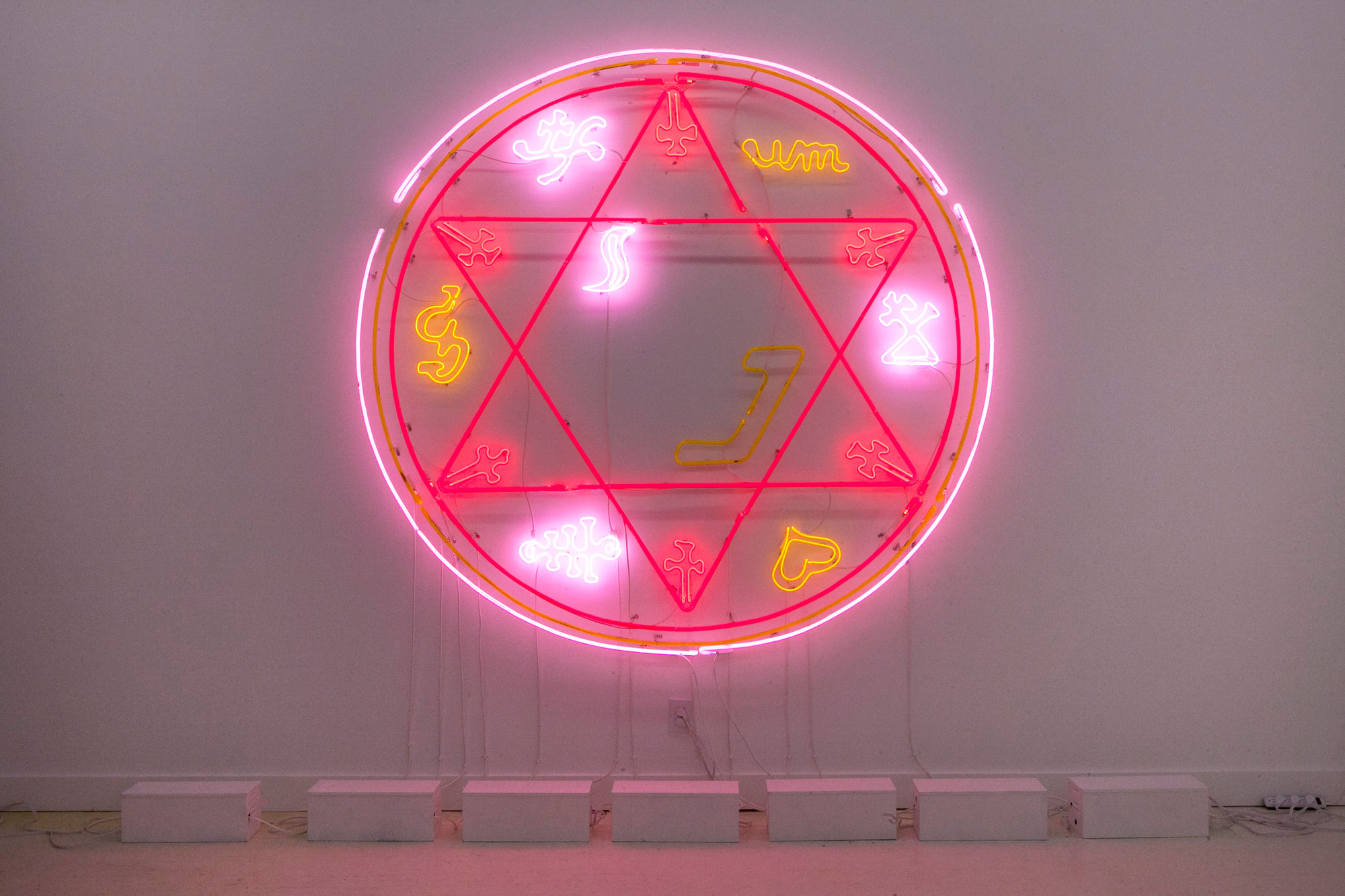 Circular neon wall piece with six-pointed star pattern, yellow, pink and red symbols