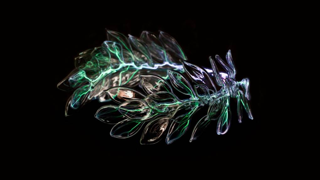 Clear glass sculpture of crown of leaves against black backdrop with green electrical current running through