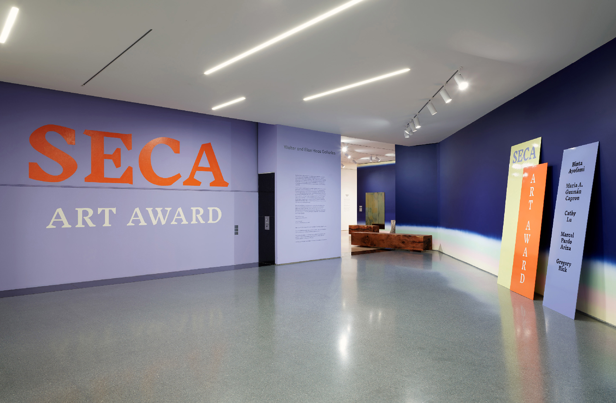 Purple gallery walls with large text of exhibition name in orange