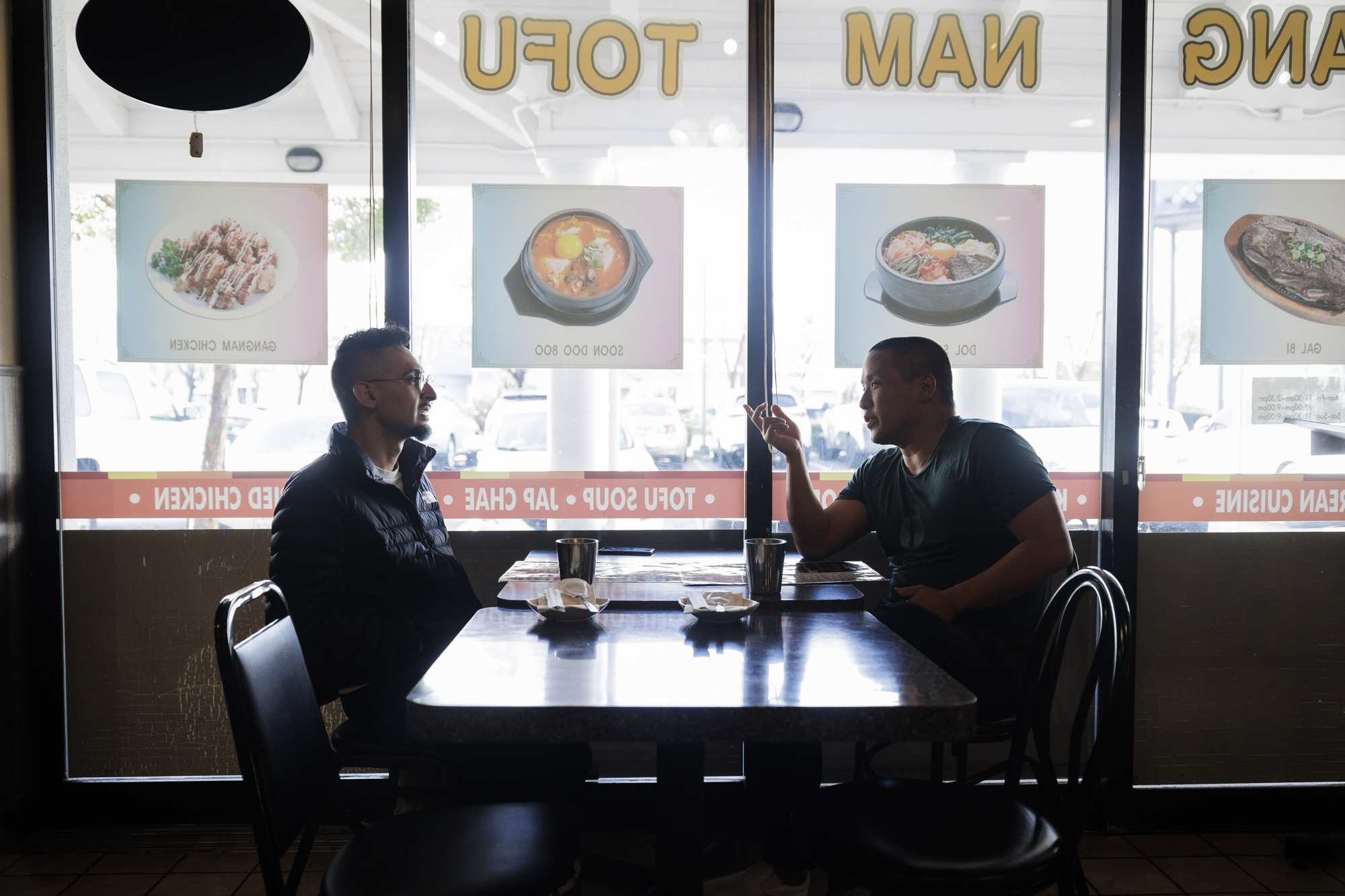 Two men seated across from each other inside a Korean restaurant.