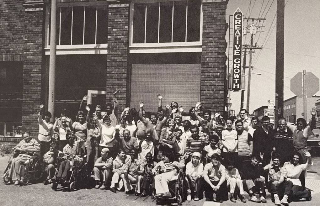 Big group photo outside brick warehouse, lots of smiling