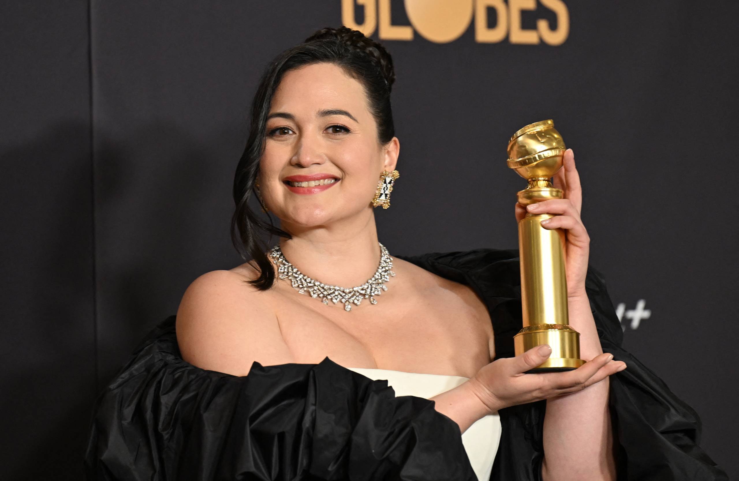 An Indigenous woman smiles and holds up a gold trophy. She is wearing a black and white gown.