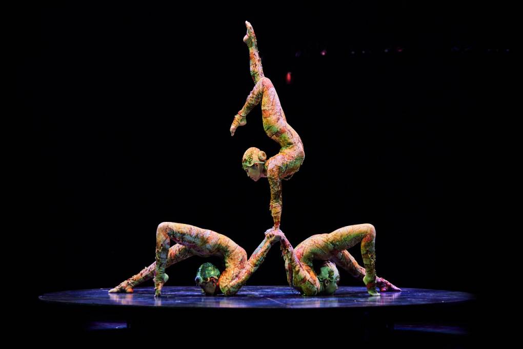 Three women in leotards contorting their bodies into a balancing pose.