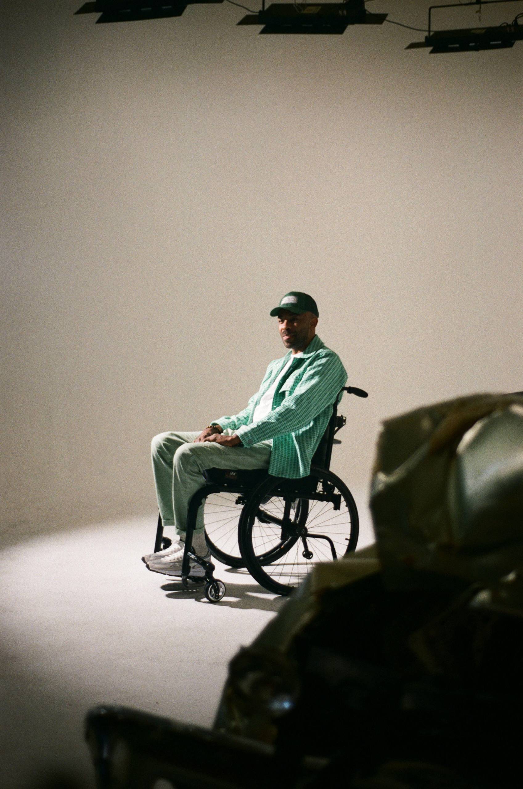 The shadow of Kwudi Hodge's hat brim covers his face as he sits on the set of his music video "Fast Car".