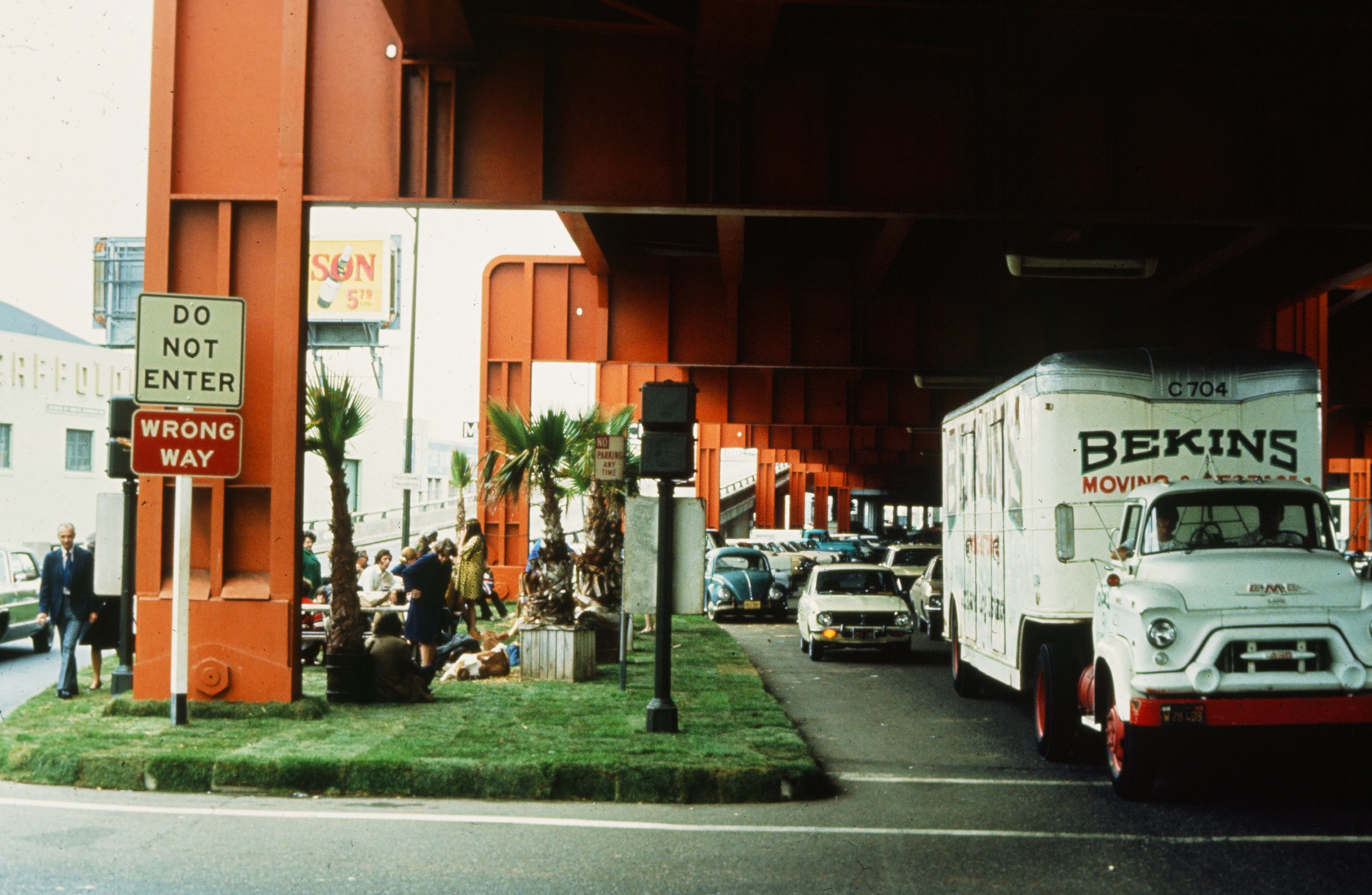 Photograph of landscaped park underneath freeway, Bekins truck in lane beside the grass