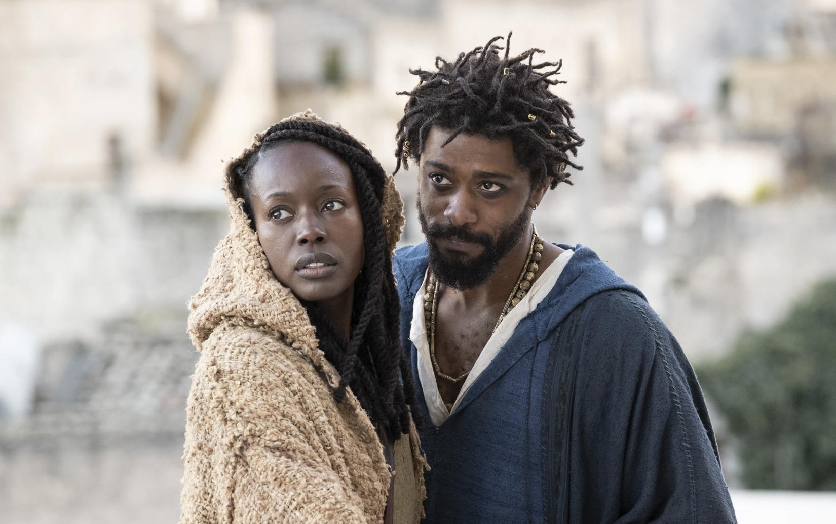 A Black woman stands close to a Black man. They are both wearing robes as if in biblical times.