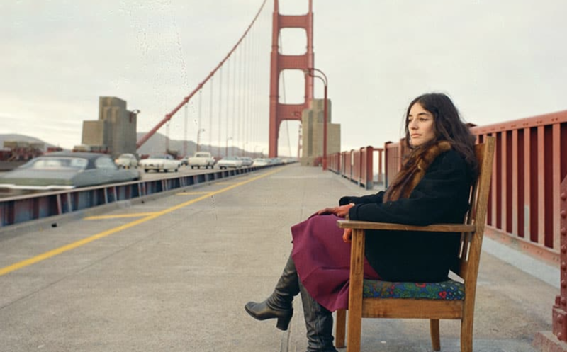 A woman sits in a dining chair on the Golden Gate Bridge, watching the traffic go by.