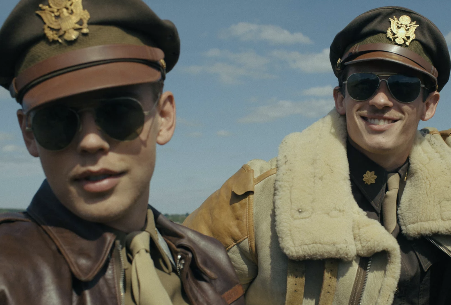 Close up of two 1940s-era pilots stand on the tarmac under blue skies.