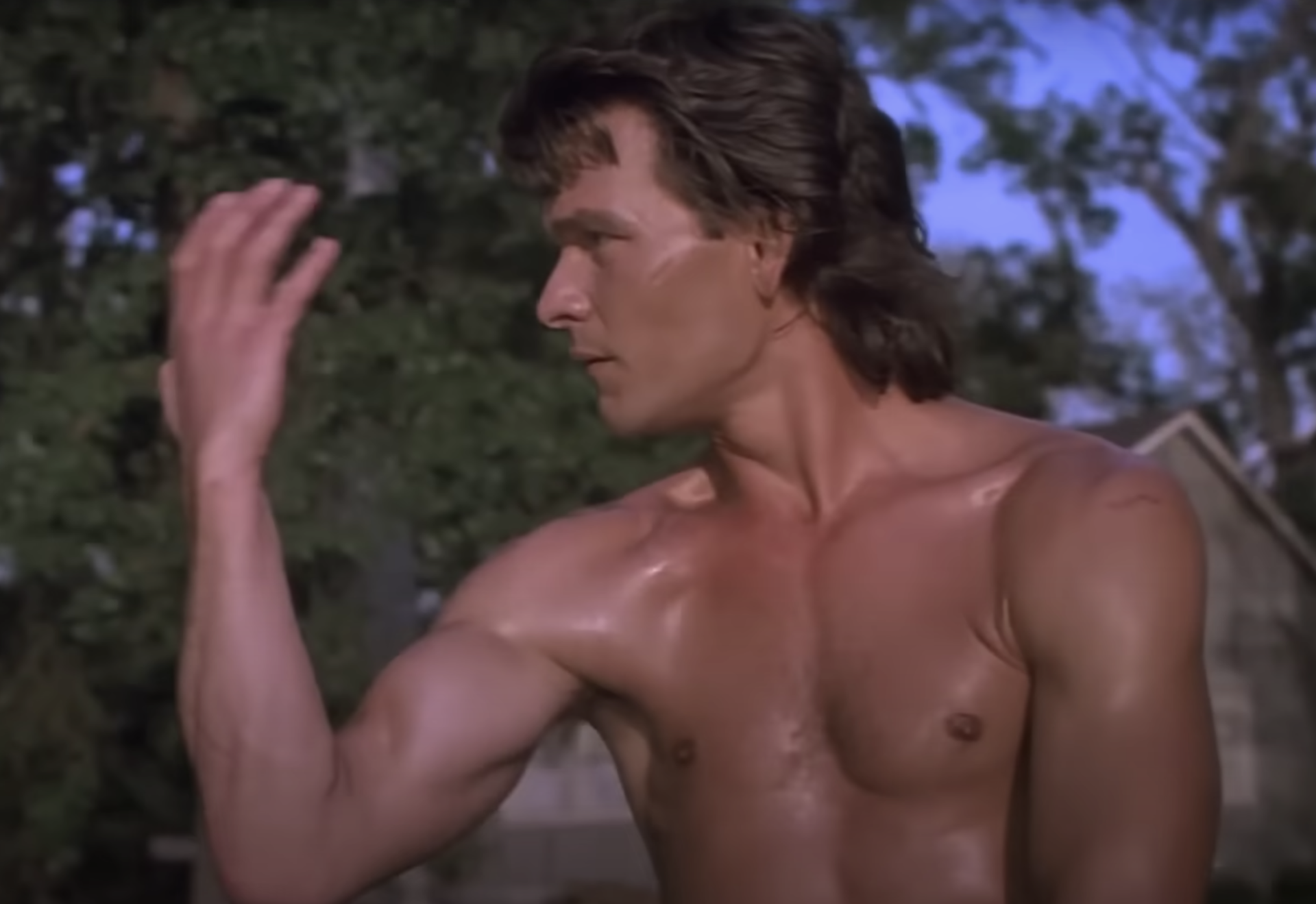 A shirtless white man practices tai chi outdoors.