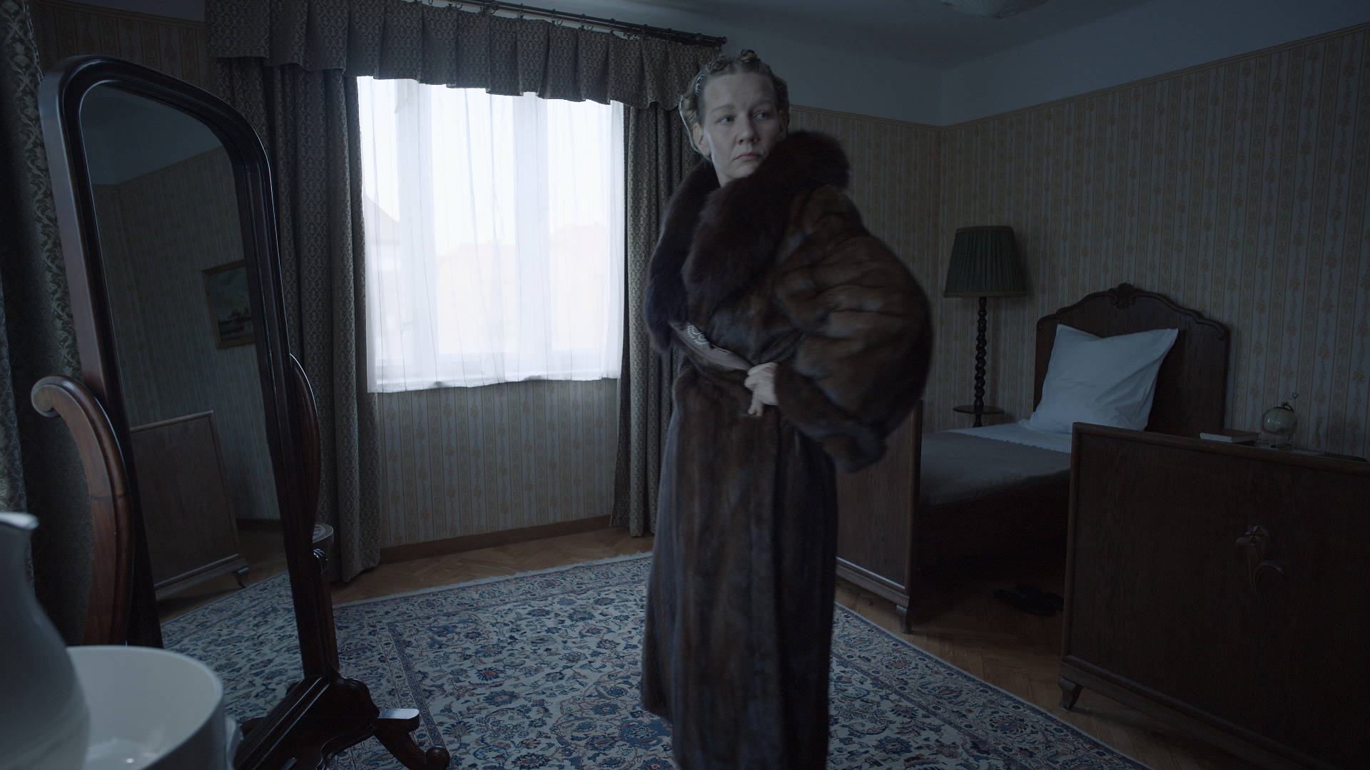 Woman poses wearing a long fur coat in bedroom