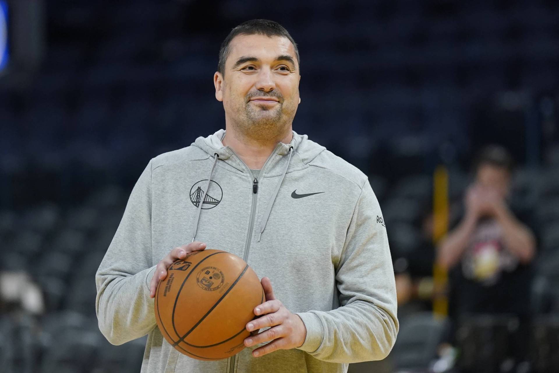 A man wearing a gre hoodie stands on a court holding a basketball.