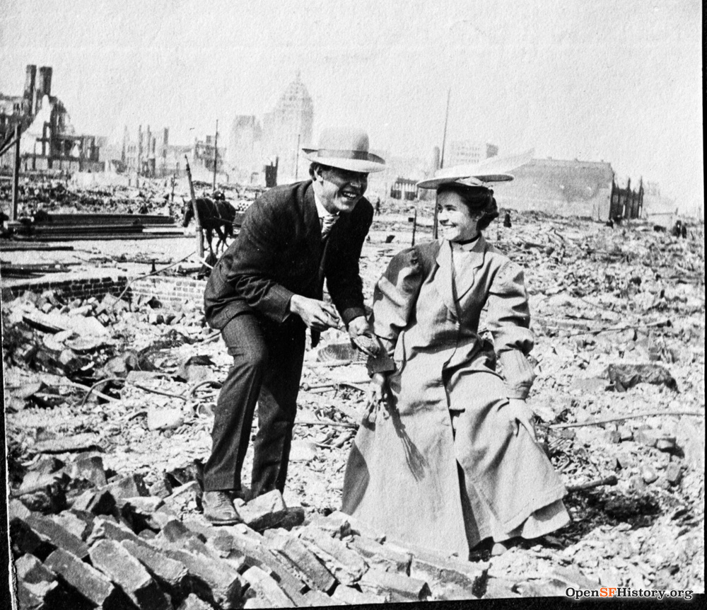 A Victorian couple gazes at each other and smiles while walking across piles of bricks and ruins.