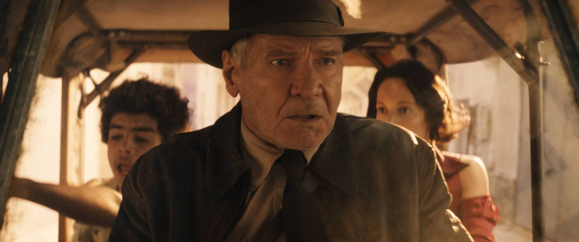 An older white man wearing a distinctive hat sits in a vehicle looking worried. Behind him, a woman and tween child sit.