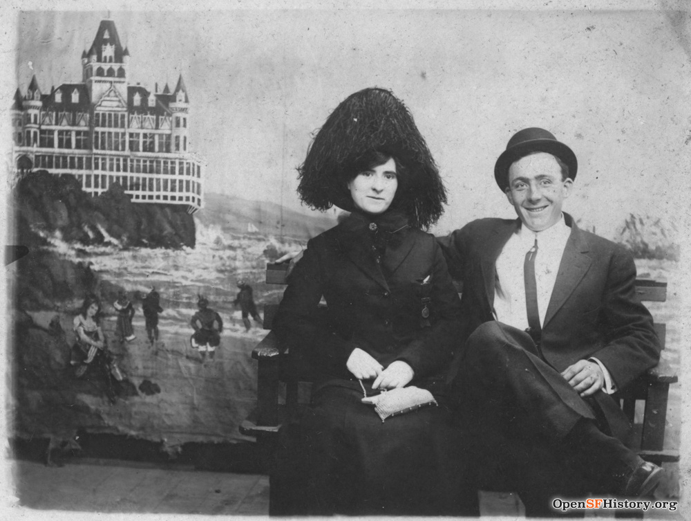 A Victorian couple sits in front of an image of San Francisco's Cliff House. 