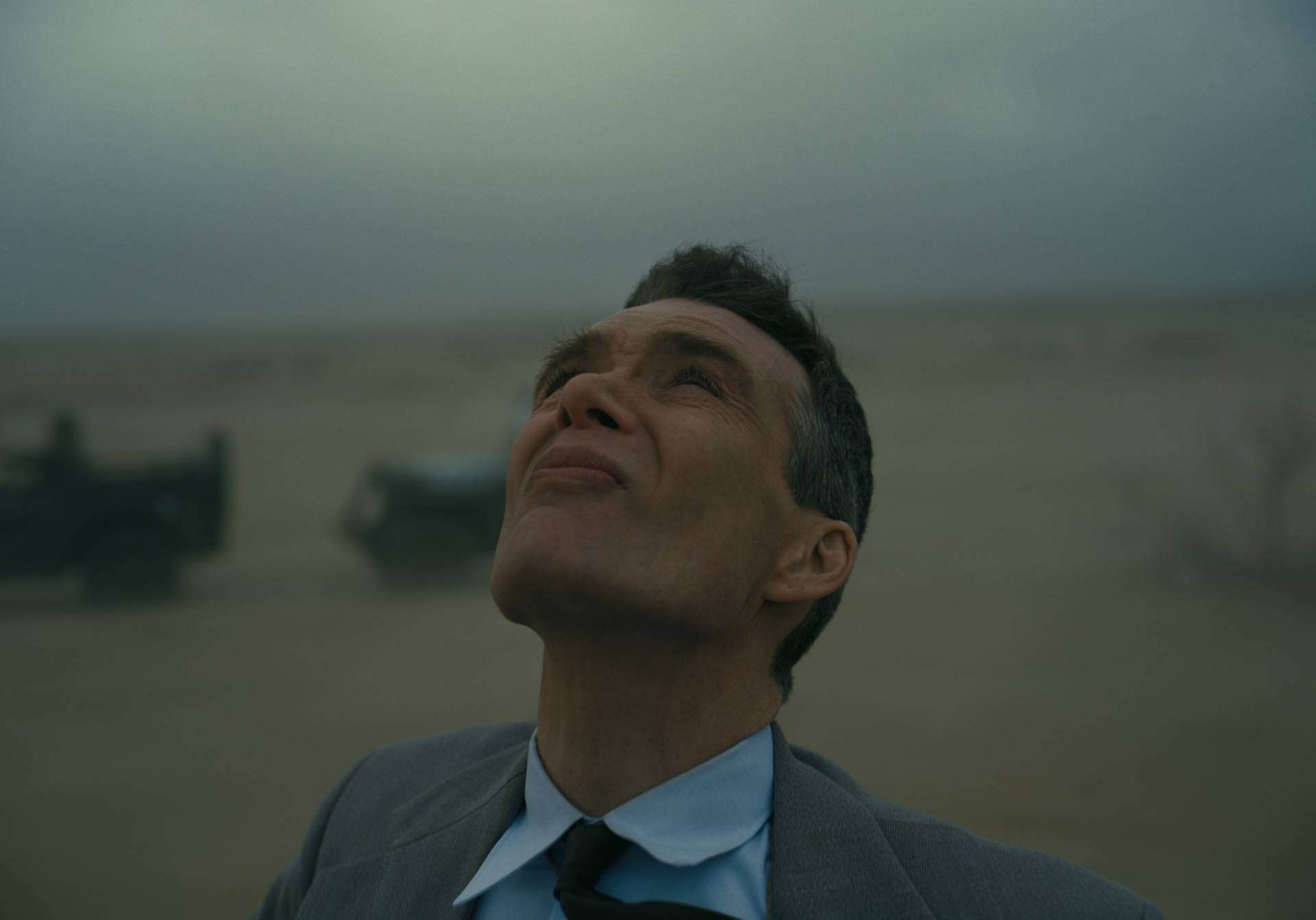 A white man wearing a suit stands in the desert and gazes up at the sky.