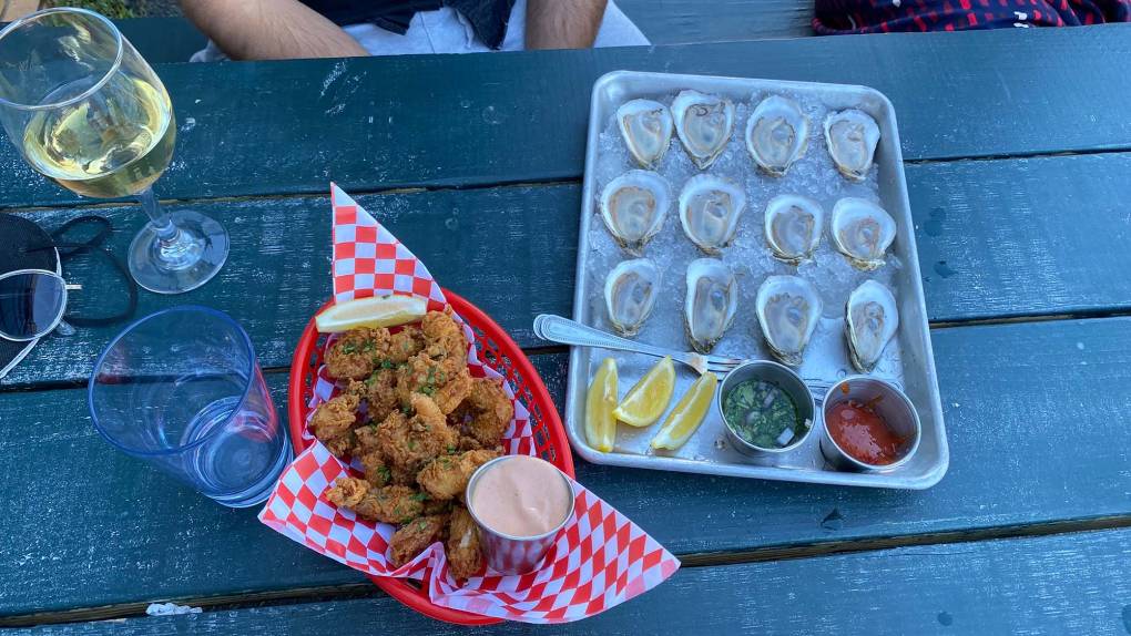 A tray of raw oysters on the half shell and a basket of fried shrimp on a picnic table.