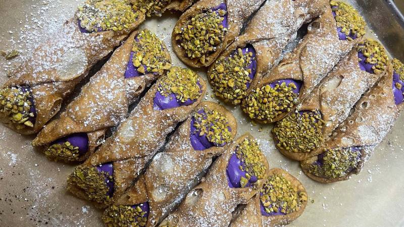 a tray of ube-flavored cannolis with pistachio crumbs