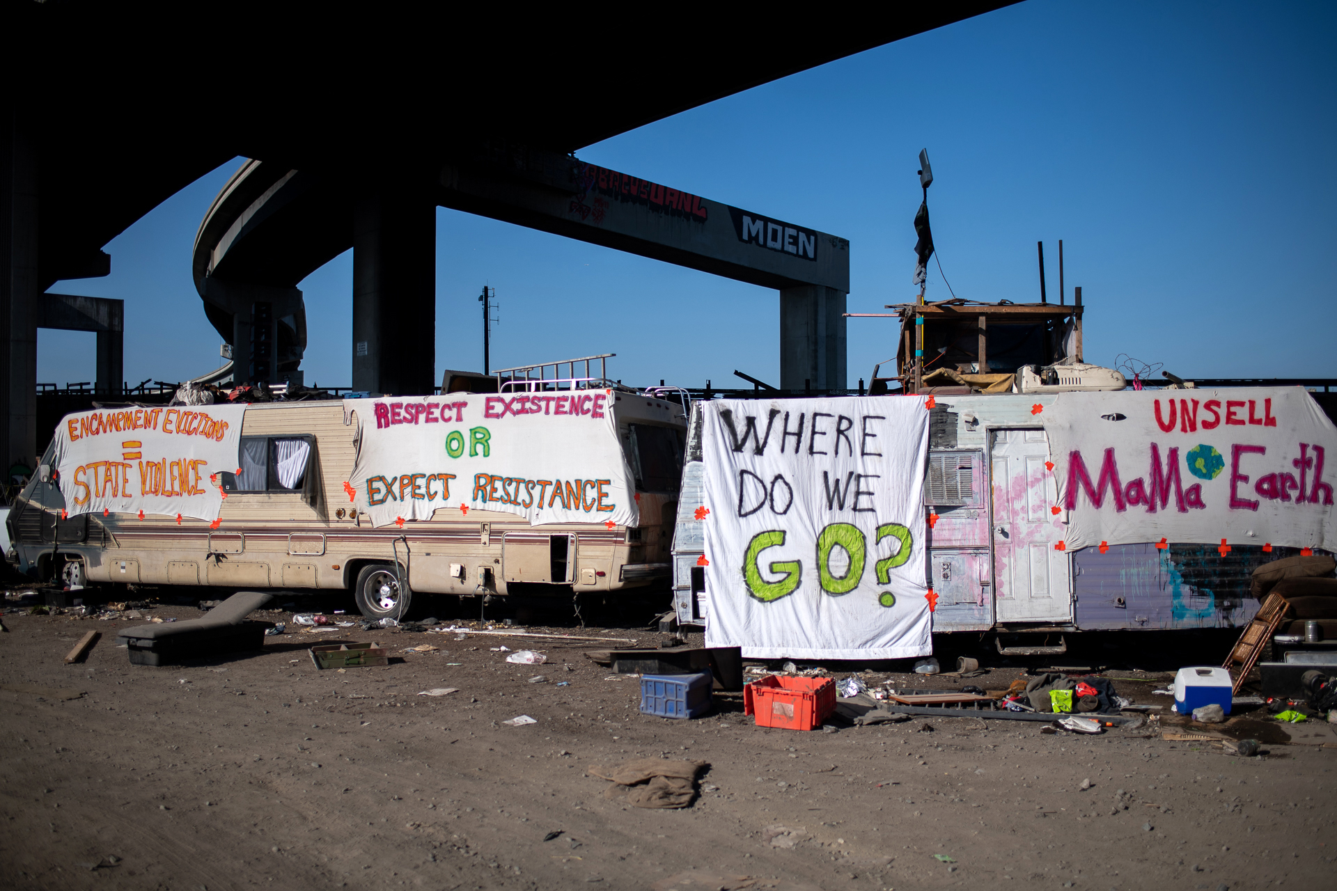 RVs in an encampment with signs that read "Where do we go?" and "Respect existence or expect resistance."