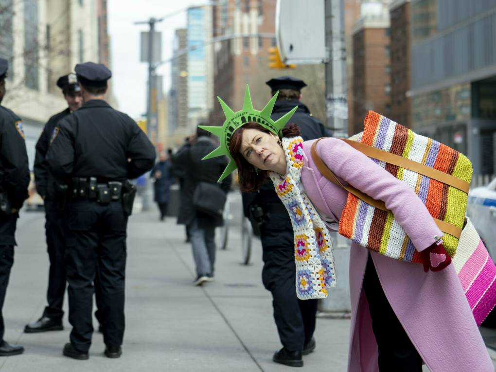A sidewalk scattered with police officers. A colorfully dressed woman peers in front of them, playfully.