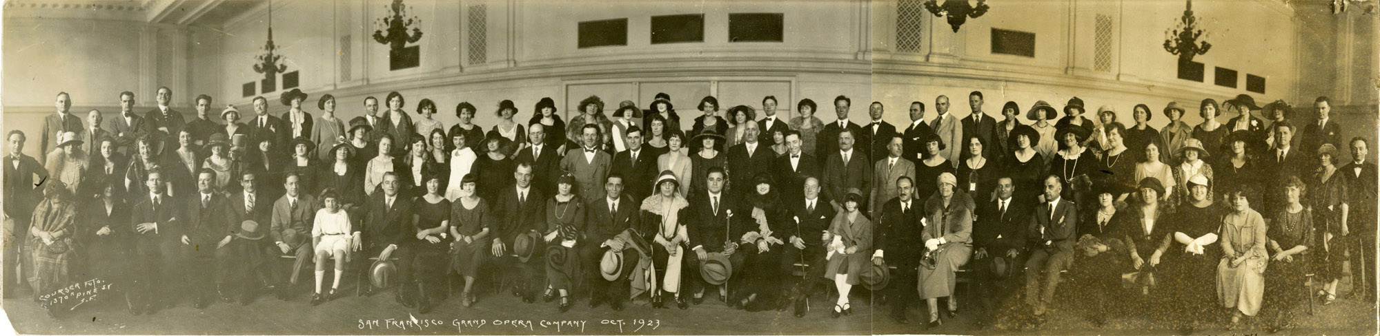 Large sepia-toned group photo of men, women and children on risers inside high-ceilinged space