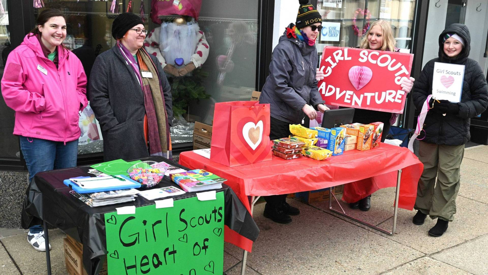 Cold parents and young people stand behind tables selling girl scouts cookies.