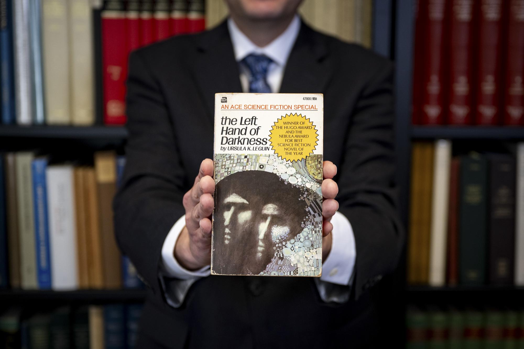Person on suit holds a paperback book in front of them with two hands