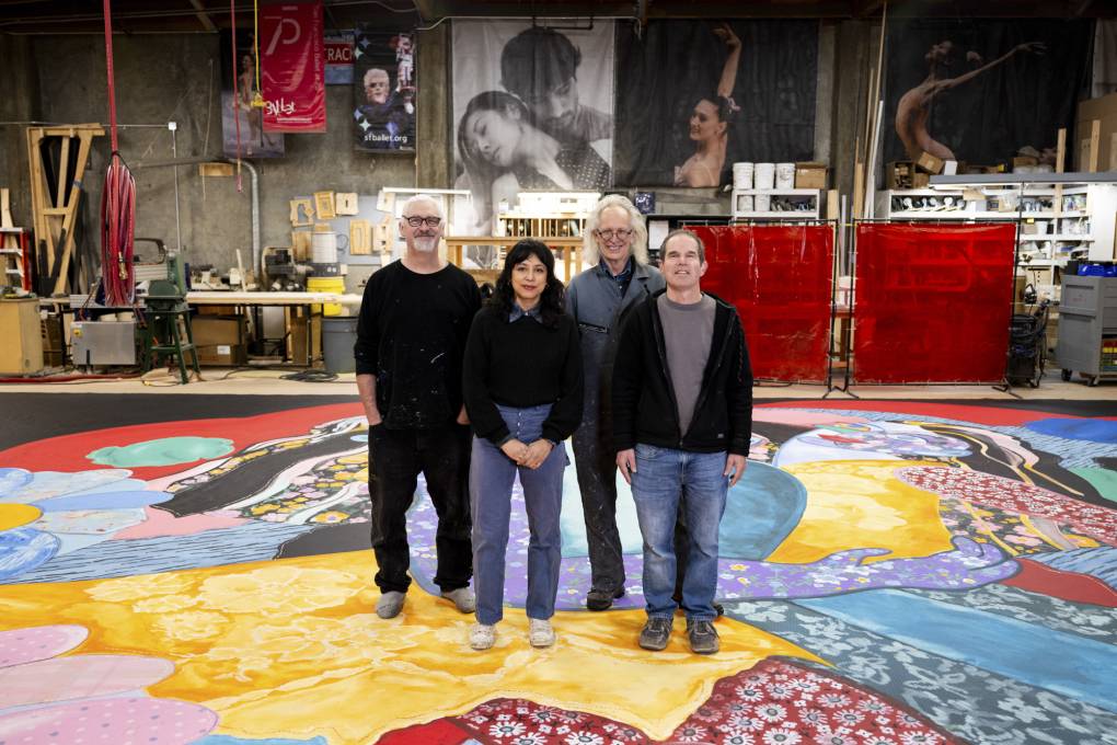 Four people stand on large painted canvas on warehouse floor