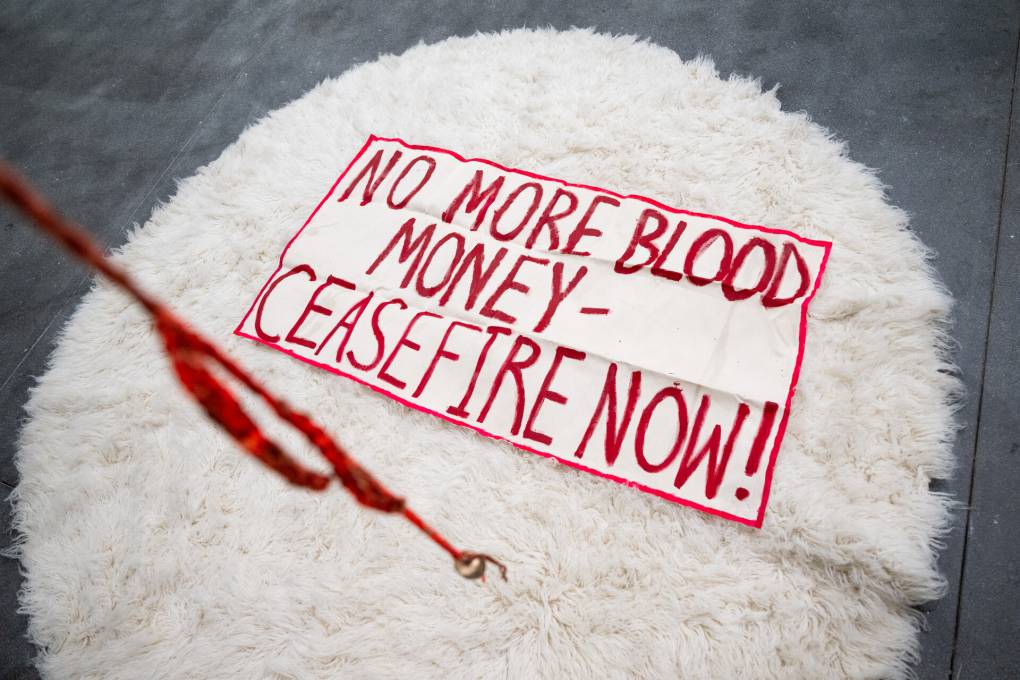 A sign over a wool rug reads "No More Blood Money - Ceasefire Now!"