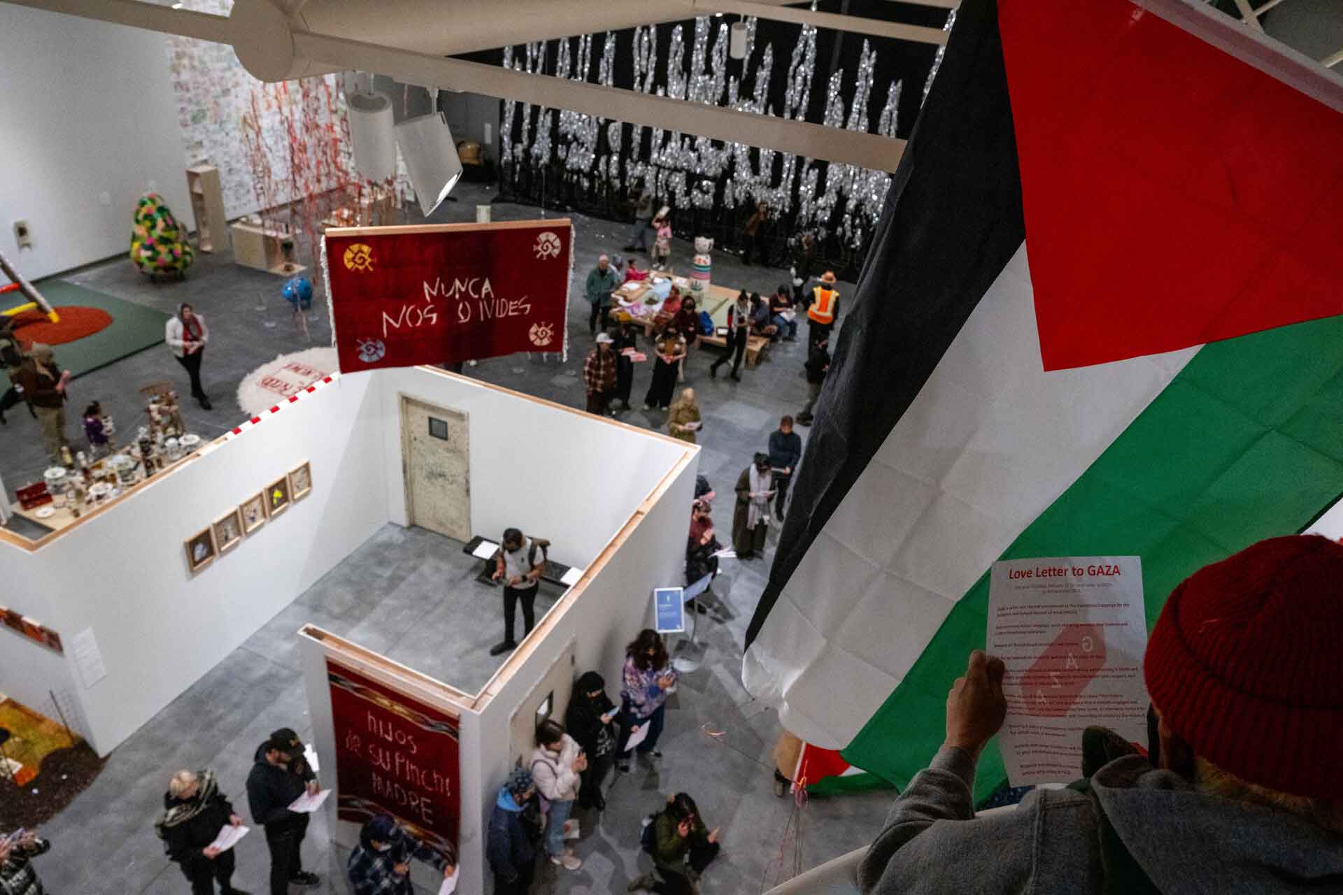 an overhead view of a museum gallery full of artworks, with a Palestinian flag hanging to the right