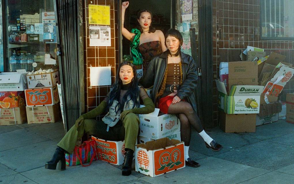 A trio of first-generation Asian American women pose in front of a Chinatown market