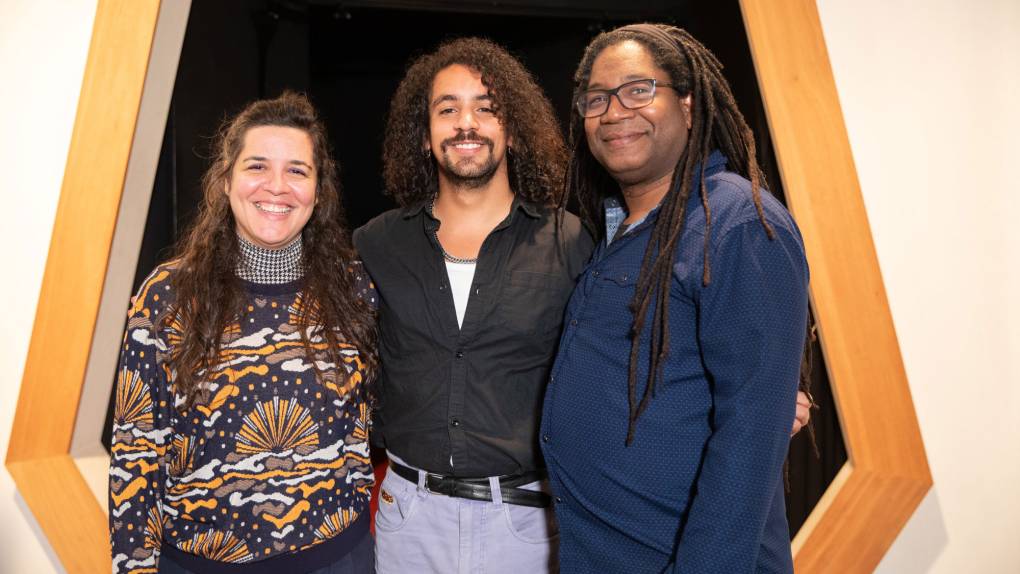 Three people stand smiling in front of angular, portal-like doorway
