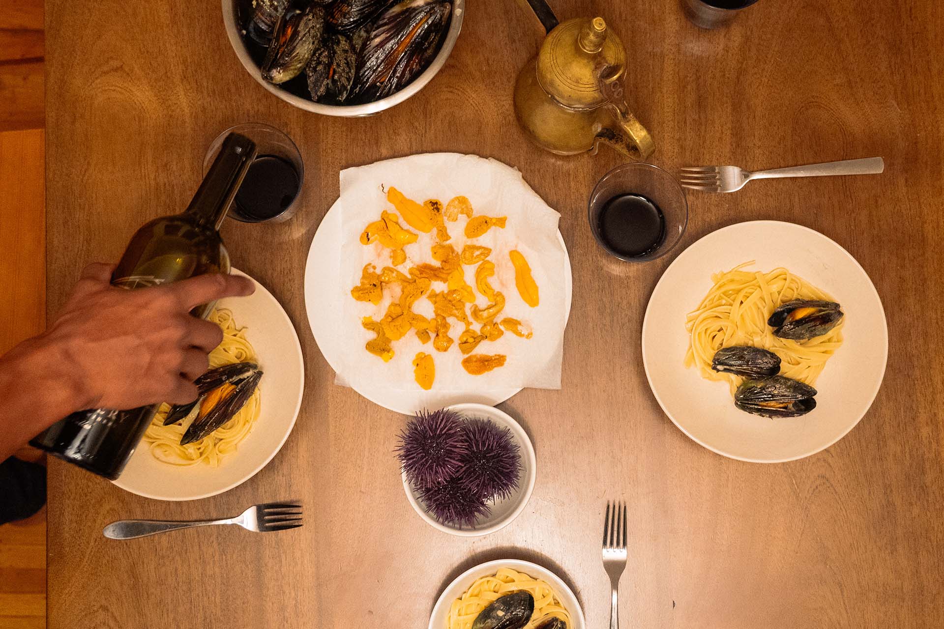 Overhead view of a sea urchin feast: individual portions of seafood pasta and a plate of raw uni lobes in the center.